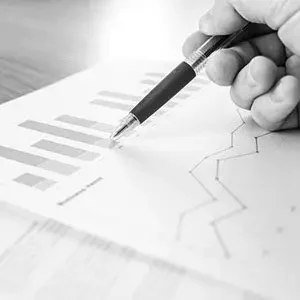 Ein Chart mit Grafiken zu einer Entwicklung ist  zu sehen. Eine Hand mit Stift zeigt auf die Grafik.